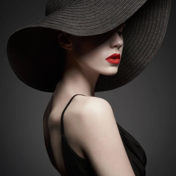 portrait of young lady with black hat and evening dress Fashion portrait of young sexy lady with beautiful black hat and evening dress. Stylish elegant woman with modern jewelry. Studio photo of pretty model on grey background.
